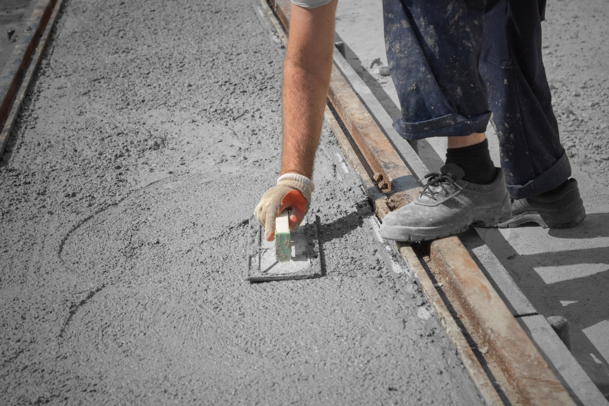 Worker using tools to flatten and finish new concrete pavement.